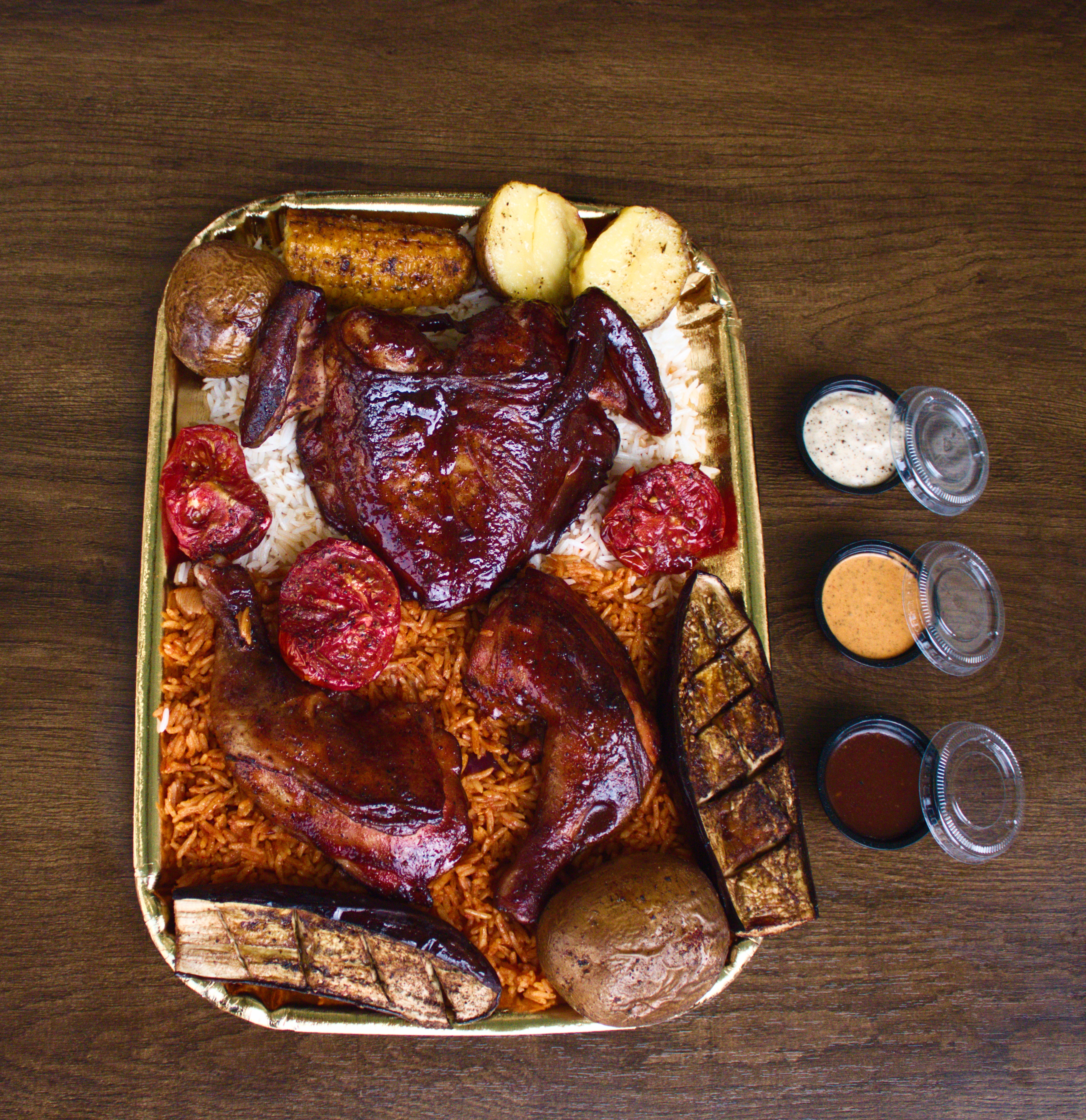 Whole smoked chicken platter with thighs, breast, and wings over red and white rice with three sauces
