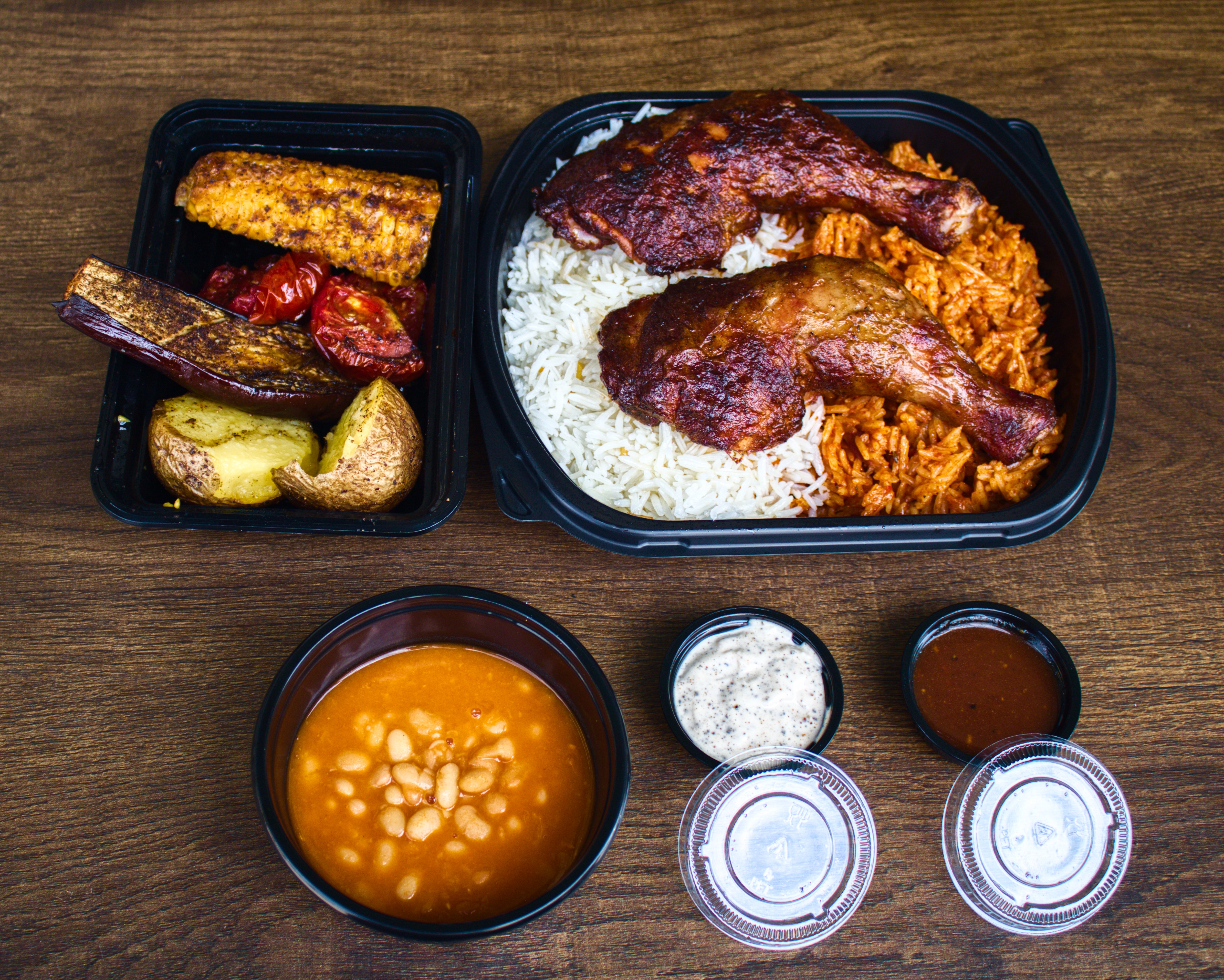 Two smoked chicken thighs over white and red rice with roasted sides